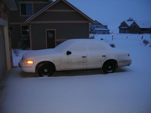 1998 Ford Crown Victoria - A white 1998 Ford Crown Victoria sedan sits covered in snow with its front turn signal illuminated.