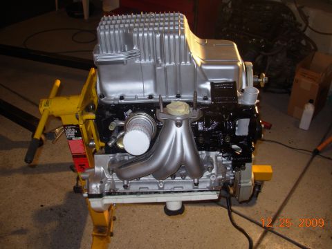 1991 Ford Taurus - Engine assembly on a stand, a silver oil pan and black block with a silver exhaust manifold.