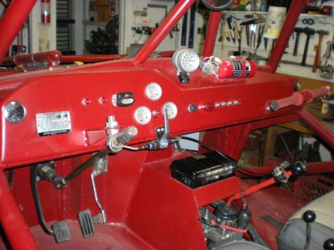 Suzuki Samurai - Interior view of a red vehicle's dashboard, multiple gauges, a fire extinguisher, and a roll cage structure.