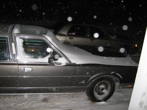 2000 Mercury Grand Marquis - A hearse and another vehicle are parked outside during a snowfall.