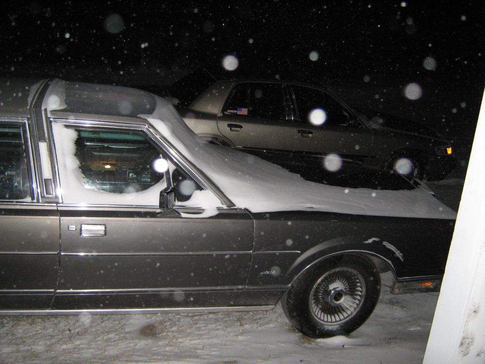 Dark hearse covered in snow, parked next to another car