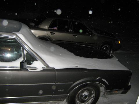2000 Mercury Grand Marquis - A gold 2000 Mercury Grand Marquis is partially covered in snow, seen from a 3q front angle.