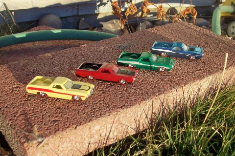 1972 Ford Ranchero - A collection of colorful toy cars are displayed outdoors on a rough, reddish-brown surface.