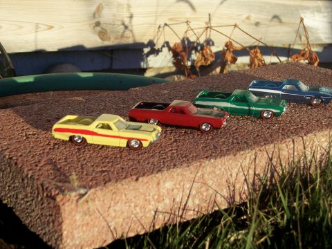 1972 Ford Ranchero - A collection of toy pickup trucks, including a yellow and red 1972 Ford Ranchero, are displayed outdoors on a textured surface.
