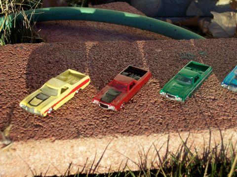 1972 Ford Ranchero - A collection of toy pickup trucks are displayed outdoors on a textured surface with grass and a green hose in the background.