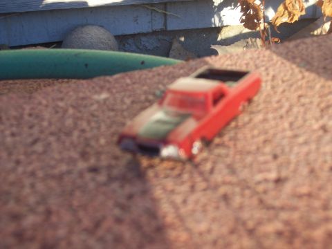 1972 Ford Ranchero - A small red toy car sits on a surface that resembles gravel or sand.