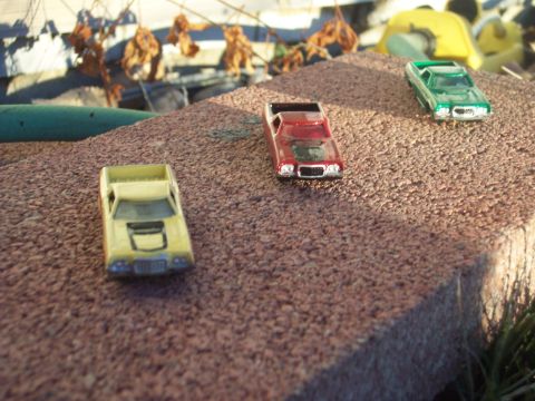 1972 Ford Ranchero - Three toy cars, including a yellow 1972 Ford Ranchero, are arranged on a textured surface outdoors.