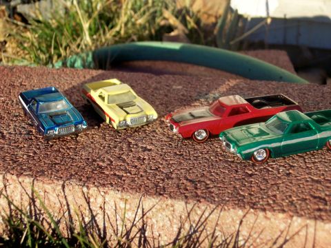 1972 Ford Ranchero - A collection of miniature vehicles are displayed outdoors on a rough, textured ground with grass and a green hose in the background.