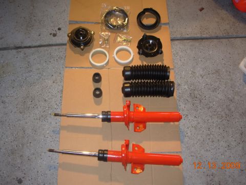 1991 Ford Taurus - Various automotive suspension components are arranged on a cardboard surface, including two struts and protective bellows.