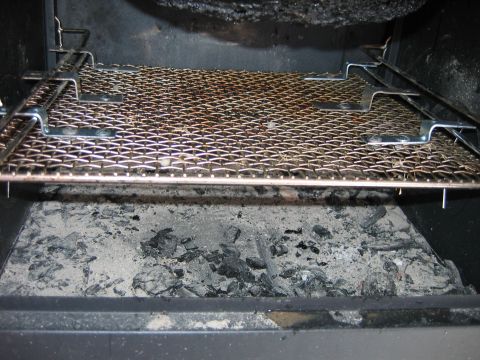 1992 Ford Bronco - The interior of a wood stove shows a metal grate positioned above a bed of ash and burnt wood.