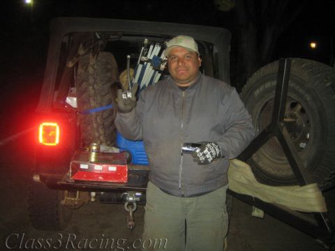 1986 Ford Bronco - Man with tools by a Jeep Wrangler, which is loaded with gear and has a spare tire on the rear.