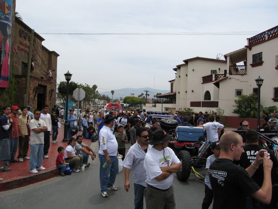 Crowd gathered on a street with several off-road vehicles, including a buggy with a blue cooler