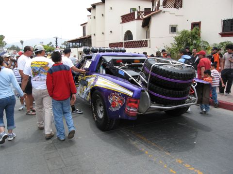 1986 Ford Bronco - A custom purple off-road truck is parked on a street with spectators gathered around.