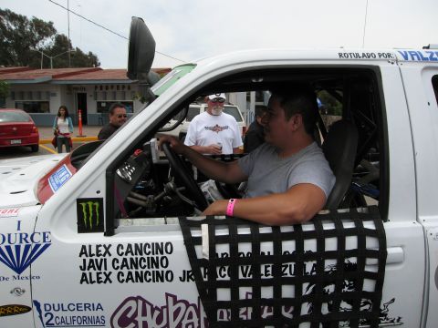 1986 Ford Bronco - Driver sits in the cab of a white off-road race truck, ready for competition.