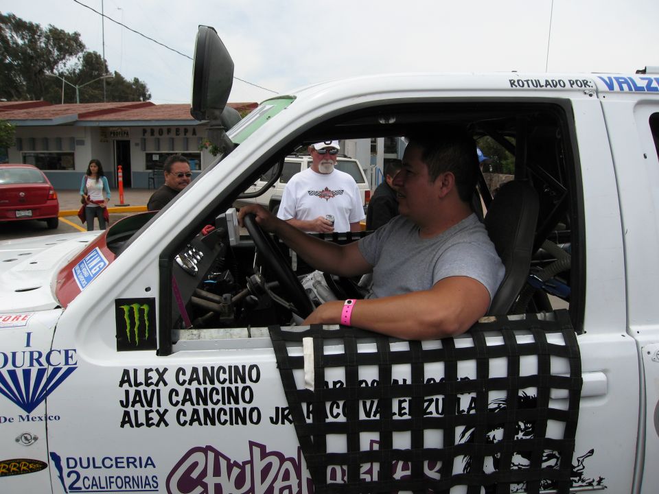 Driver in a white off-road race truck with racing decals and names on the door