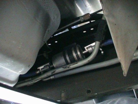 2007 Ford Mustang - Underbody view along a vehicle's frame rail showing an inline cylindrical fuel filter clamped in a black bracket, with braided and hard fue…