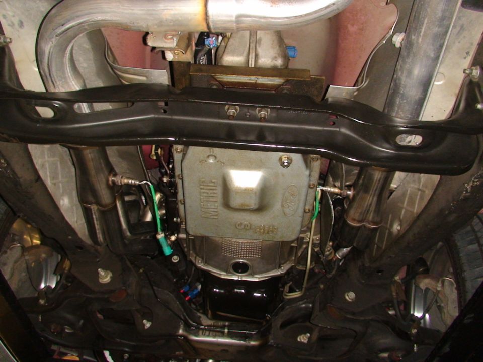 Underside of a 2007 Ford Mustang showing the transmission pan with Ford logo, exhaust pipes, and suspension components