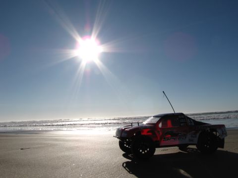 1984 Ford Bronco - A remote control truck sits on the sand near the ocean waves under a bright sun.