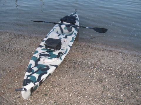 1991 Ford Bronco - A camouflage kayak rests on the shore, its paddle resting across its body.
