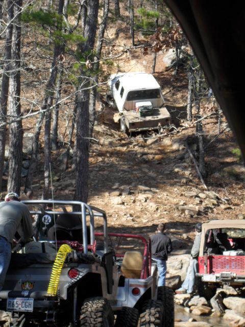 1986 Ford Bronco - Multiple off-road vehicles are seen on a challenging trail in a wooded area.