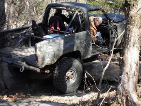 1986 Ford Bronco - This heavily modified truck, equipped with a roll cage, is shown navigating a challenging off-road course with large logs and rocks.
