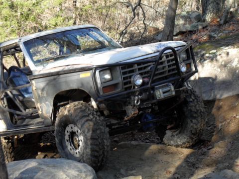 1986 Ford Bronco - This heavily modified SUV is shown tackling a challenging off-road course with large boulders.