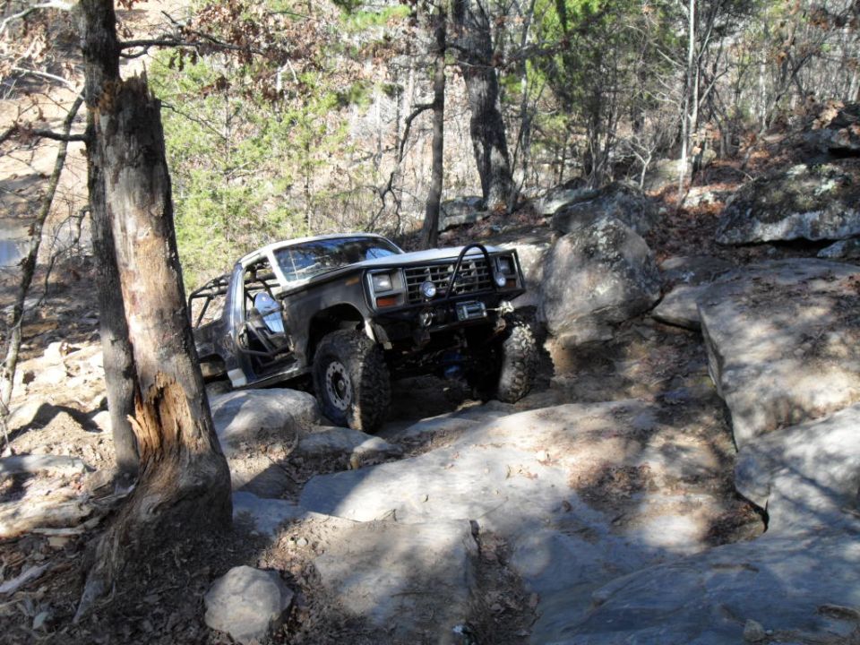 Modified dark gray Ford Bronco off-roading over rocks, with a roll cage and winch