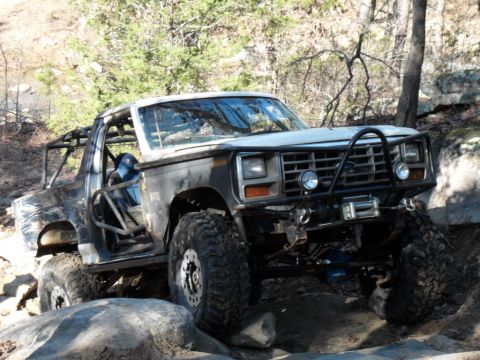 1986 Ford Bronco - This modified 1986 Ford Bronco navigates rocky terrain, its off-road capabilities with a custom roll cage and winch.