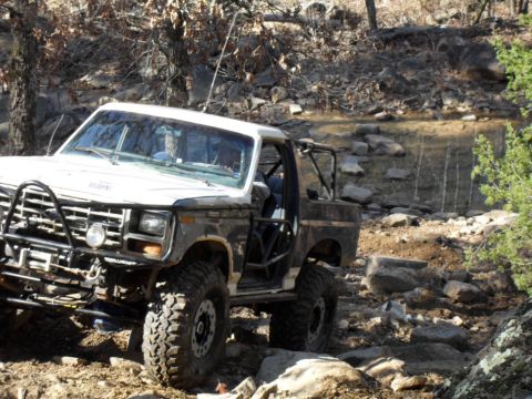 1986 Ford Bronco - Off-road Bronco navigating a rocky trail with significant suspension modifications.