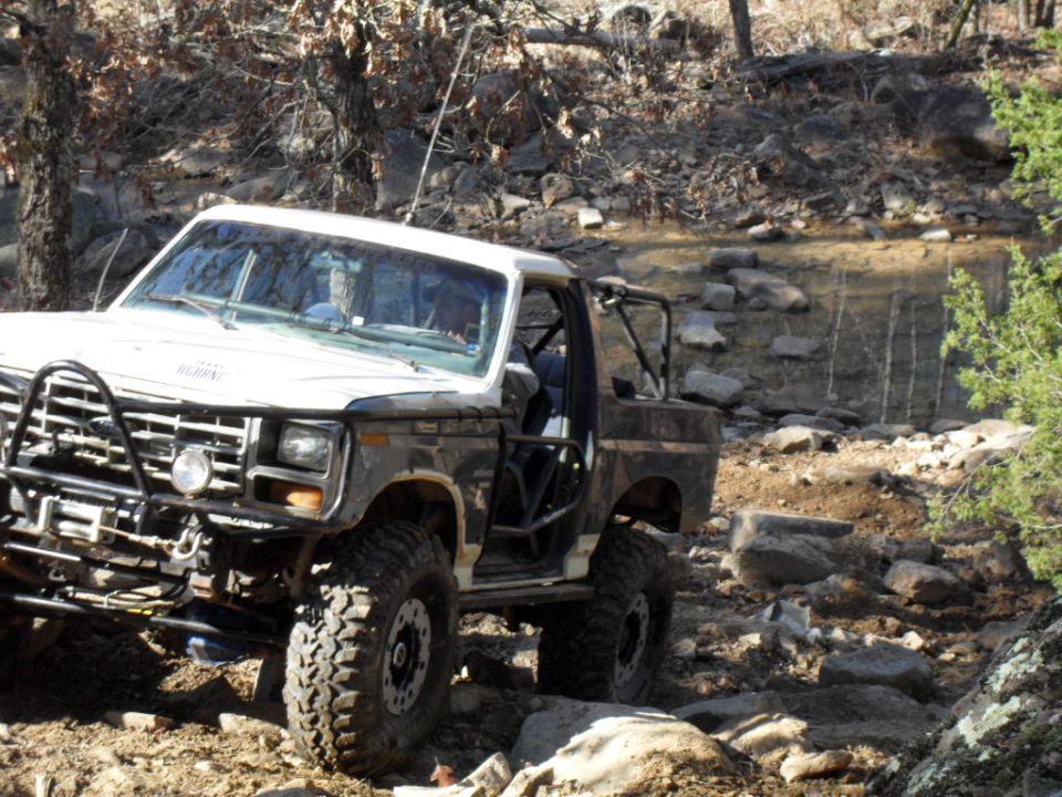 Modified 1980s Ford Bronco on rocky terrain, front bull bar, roll cage visible