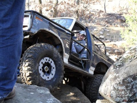 1986 Ford Bronco - This modified 1986 Ford Bronco is shown navigating a rocky trail, with the driver visible inside the modified interior.