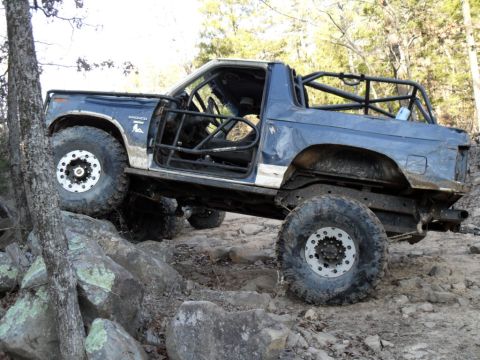 1986 Ford Bronco - Modified blue Ford Bronco navigates a rocky trail with its doors removed and a roll cage installed.