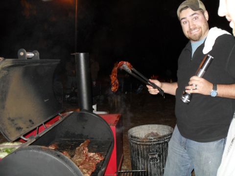 1986 Ford Bronco - A man uses tongs to flip ribs on a smoker while standing next to a trash can.