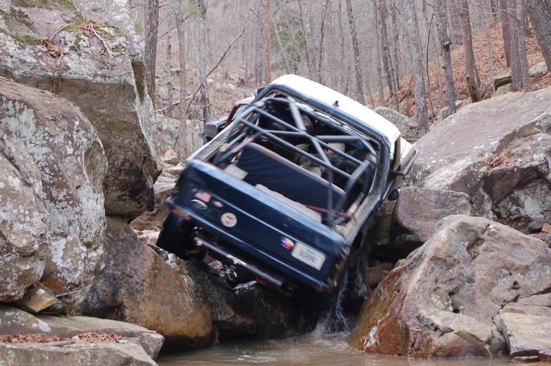 Blue Ford Bronco with roll cage climbing out of a rocky creek on an off-road trail