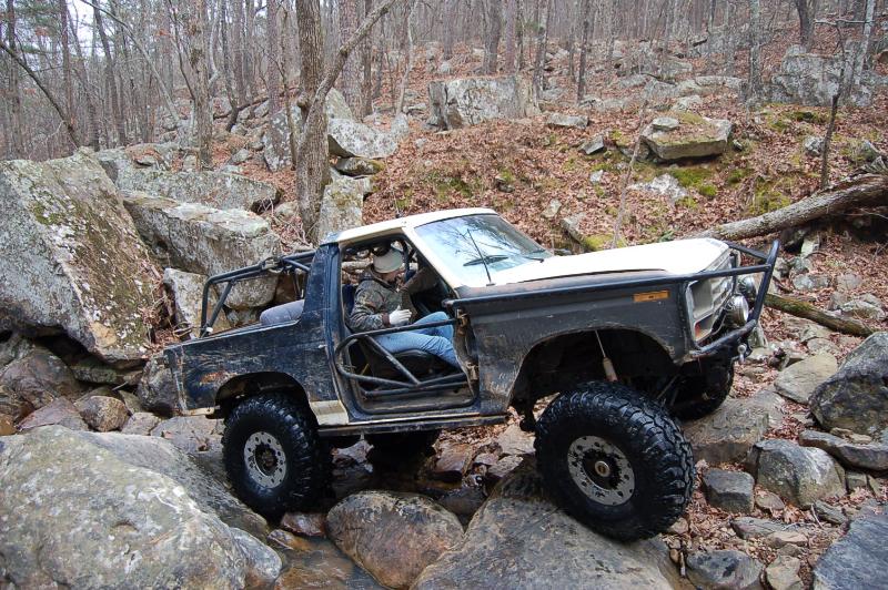 Doorless blue and white Ford 4x4 with roll cage crawling over boulders on a rocky trail