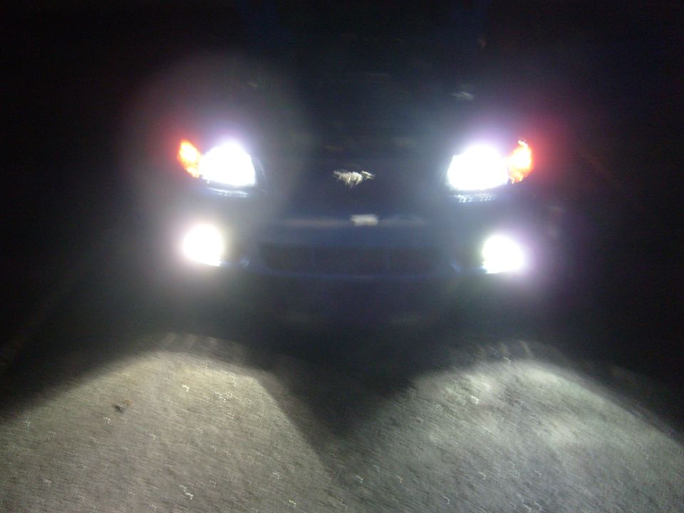 Front view of blue car at night with headlights on, showing a horse emblem