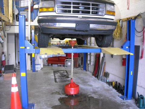 1992 Ford Bronco - A Ford truck is being serviced on a hydraulic lift in a garage, with a drain pan positioned to catch fluids.