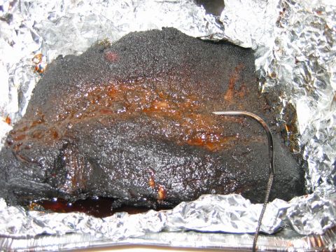 1992 Ford Bronco - A close-up view of a smoked brisket, wrapped in foil, with a thermometer probe inserted to check the internal temperature.
