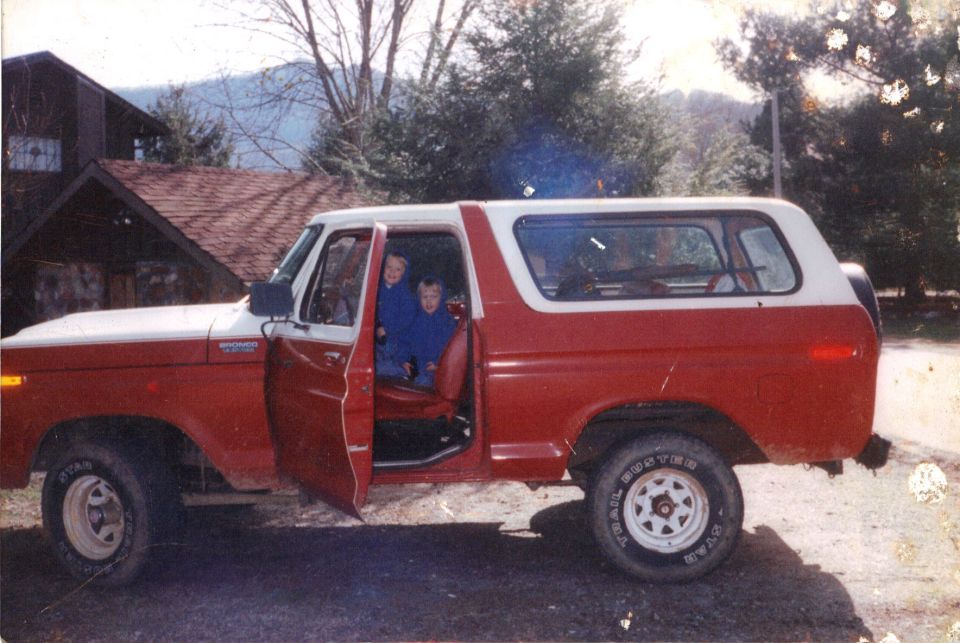 Red and white Ford Bronco SUV, side view, door open with two kids inside