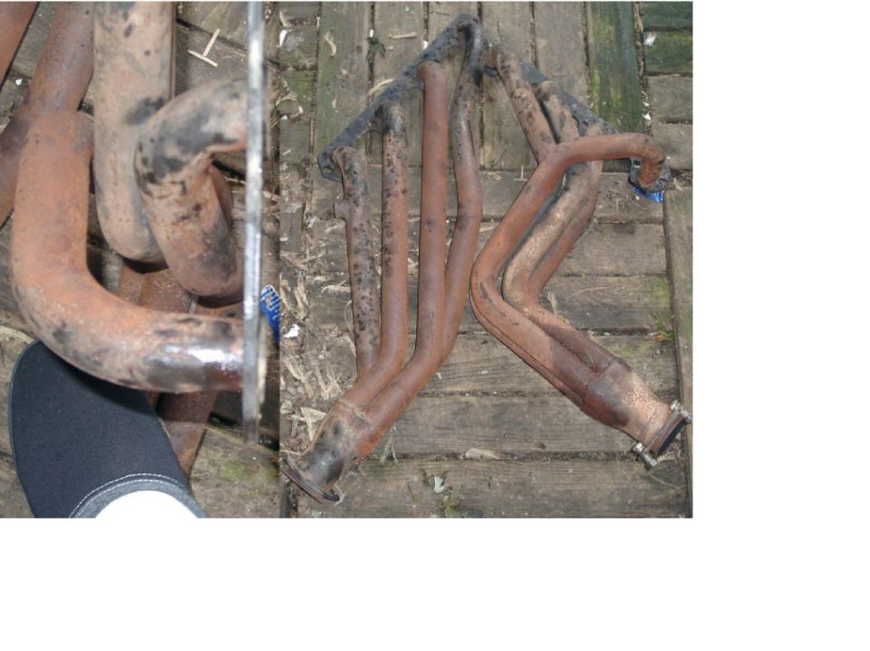 Rusty tubular exhaust headers laid out on a weathered wooden deck