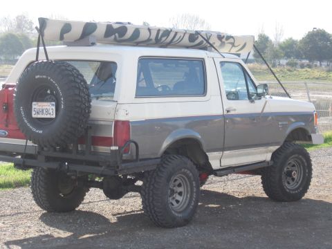 1991 Ford Bronco - 1991 Ford Bronco with a camouflage kayak secured to its roof rack and a spare tire mounted on the back.