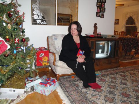 2000 Ford Crown Victoria - A woman sits in an armchair in a living room decorated for Christmas, with a tree and presents visible presents visible.