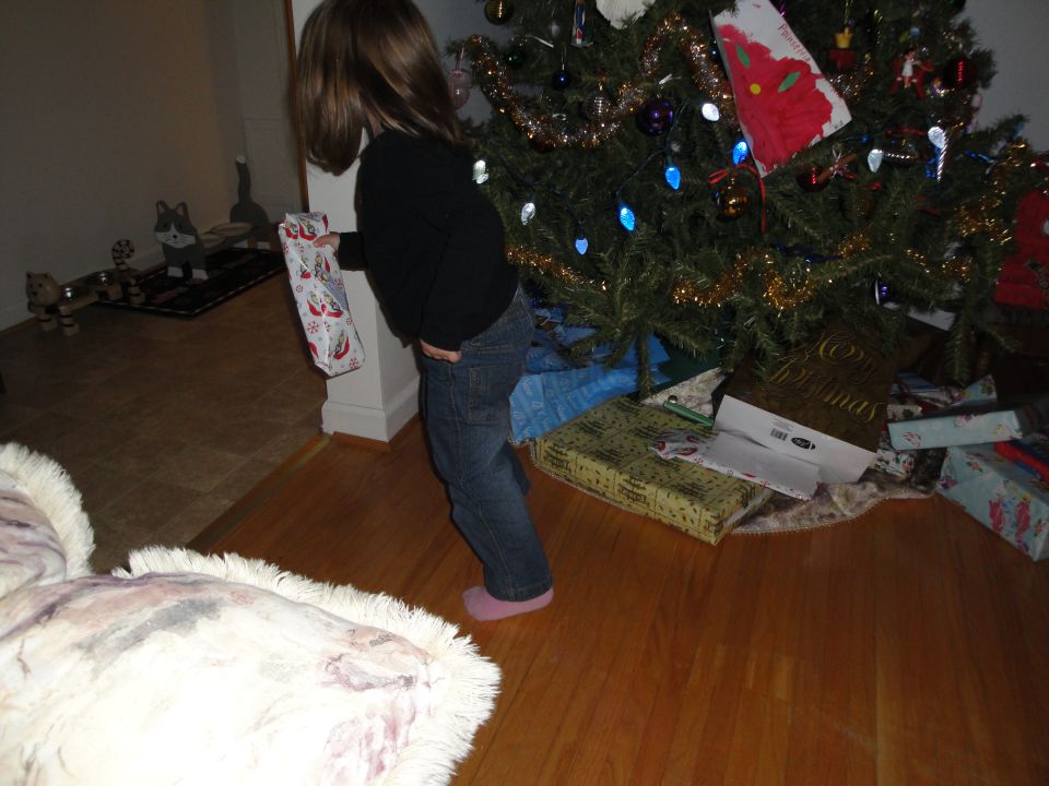Child holding a gift near a decorated Christmas tree with presents underneath