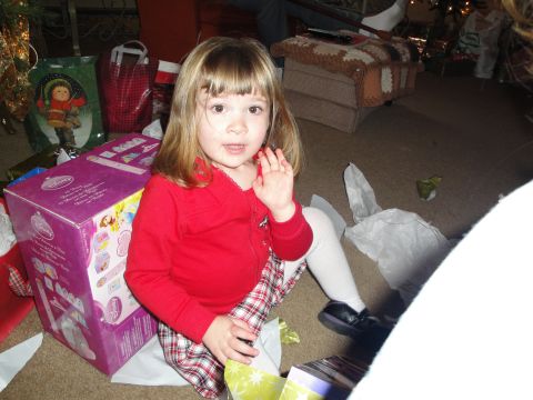 2000 Ford Crown Victoria - A young child sits on the floor, surrounded by gifts and wrapping paper, waving a hand.