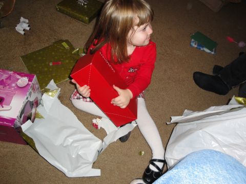 2000 Ford Crown Victoria - A young girl in a red sweater opens a large red gift box on Christmas morning, with other presents scattered around her.