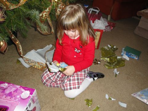 2000 Ford Crown Victoria - A young girl sits on the floor, unwrapping a gift next to a decorated Christmas tree and scattered wrapping paper.