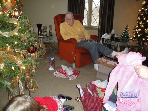 2000 Ford Crown Victoria - An elderly man sits in a chair near a decorated Christmas tree, surrounded by gifts and a child.