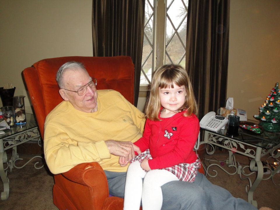 Man in yellow shirt sits in orange chair holding hands with a young girl in a red top and plaid skirt