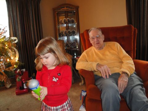 2000 Ford Crown Victoria - A young girl plays with a toy microphone while an elderly man watches, with a Christmas tree in the background.