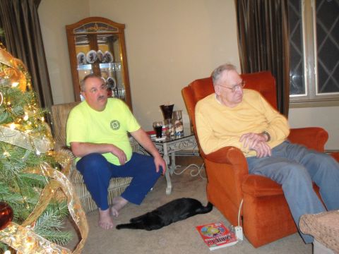 2000 Ford Crown Victoria - Two men relax in a living room with a Christmas tree and a black cat on the floor.